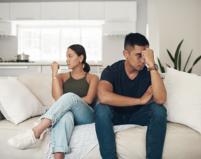 Image of a couple sat on a sofa looking unhappy and turned away from each other.