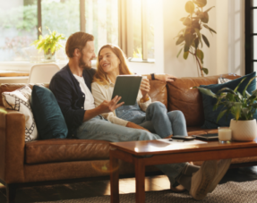 Photo of a cohabiting couple sitting on a sofa together with a tablet.