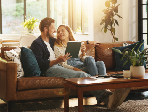 Photo of a cohabiting couple sitting on a sofa together with a tablet.