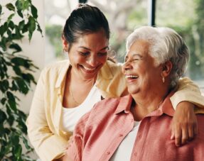 Image of a younger woman with her arm around an older woman, both of them happy and laughing.